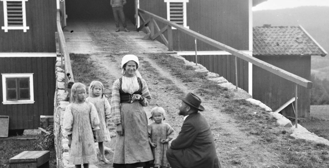 Et av de mer kjente bildene fra reisen i 1910 ble tatt i Heddal. Albert Kahn (t.h.) var på hele reisen raus med gaver til barn de møtte. Det vanket både sukkertøy, sølvringer og pengegaver. Her er han såkalt snikfotografert av Wilse mens han gir gaver til barna på Heddal prestegård. Foto: A.B. Wilse/NB.