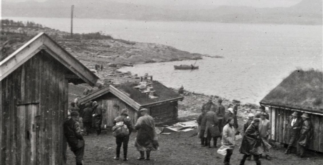 Mennesker står ved bygninger ved vannkanten til innsjøen Møsvatn. På vannet sees en snekke.  Foto: NIA