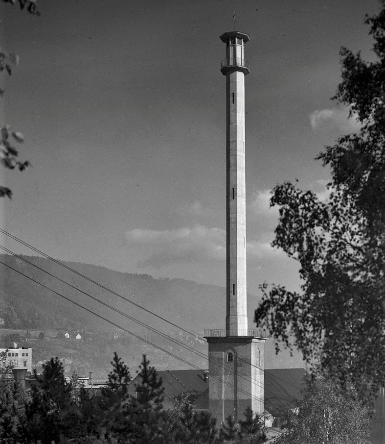Bygg 135 – Minareten Oppført: 1927-28 (Arkitekt: Thorvald Astrup). Tårnet ble oppført som luftinntak til nitrogengassproduksjonen i ammoniakkprosessen. Dette var et nødvendig tiltak ettersom lufta rundt fabrikkene inneholdt forurensninger (Acetylen) som skapte eksplosjonsfare. Rein luft ble fraktet i rør inn til nitrogenfabrikken. Det 63 meter høye tårnet står inntil Emballasjefabrikken (bygg 140), og er forbundet med gangbru til Kalksalpeterfabrikken (bygg 105). Minareten er et landemerke på Notodden. (Foto: H. Johnsrud/NIA).