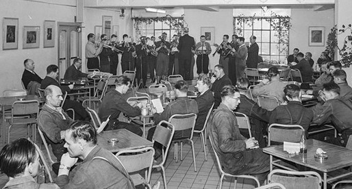 Nye takter, nye toner: Musikkorpset spiller julen inn. Det er 24. desember 1954 på den nye velferden (spisesalen) i den gamle kalksalpeterfabrikken. Men fortsatt har arbeiderne i fabrikken med både egen matpakke og kaffeflaske. (Foto: Hydro/NIA).